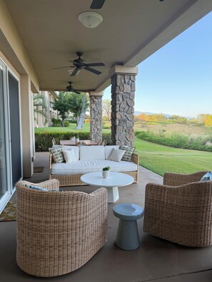 A covered outdoor seating area with wicker furniture, a ceiling fan, and a view of a landscaped garden. - The Azure at Mauna Kea: Relaxed Luxury + Ocean Views + Resort Option (Kamuela)