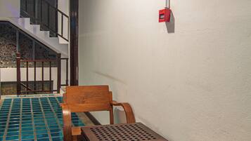 A room with a wooden table and chairs, a patterned floor, a staircase, and a wall-mounted fire alarm.