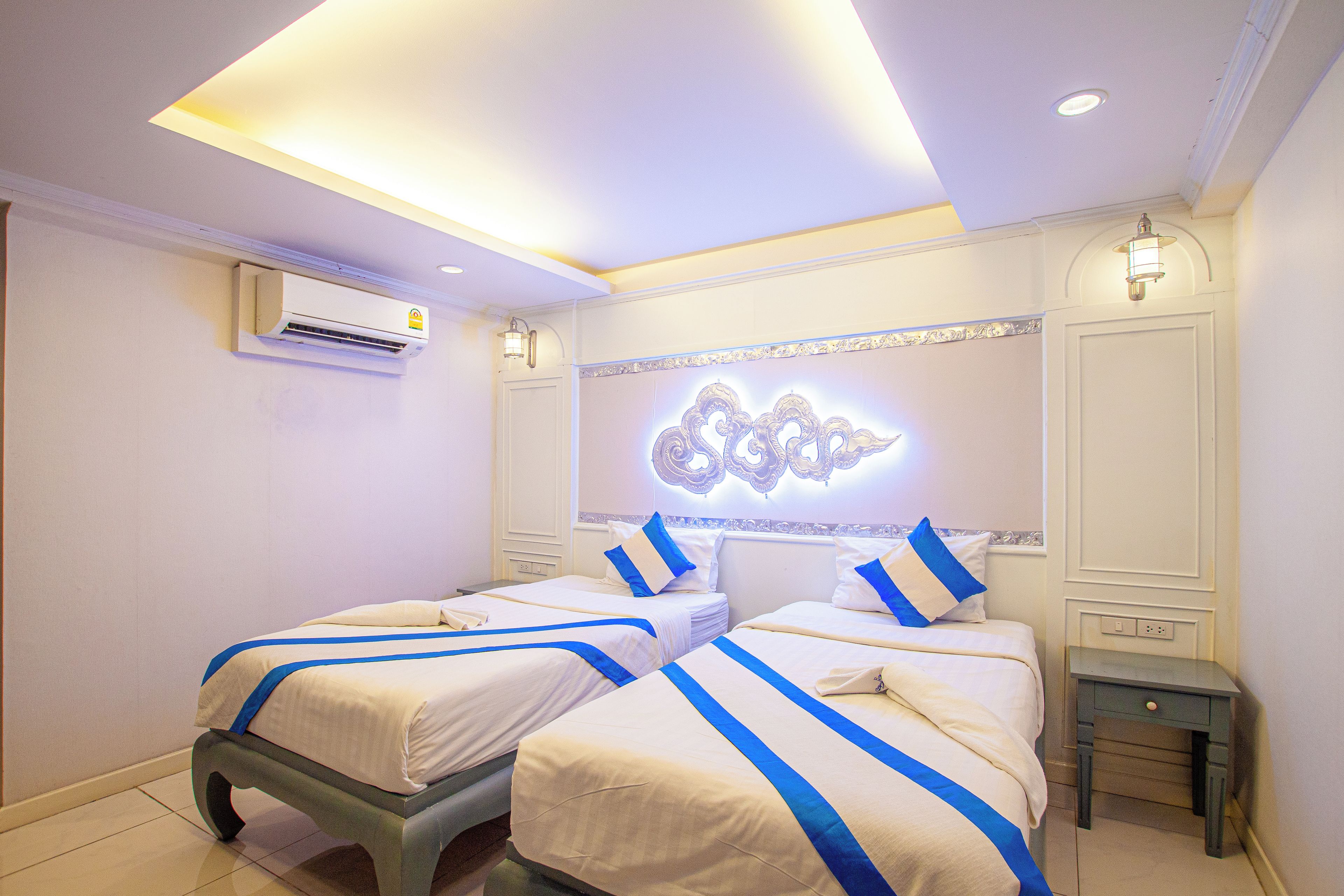 Habitación de hotel con dos camas, una lámpara en el techo, aire acondicionado y un adorno en la pared.