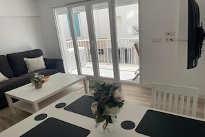 A modern living room with a sofa, a coffee table, and a dining table with a vase of flowers. - Apartment on the beachfront in La Fossa with ocean and pool views. (Calpe)