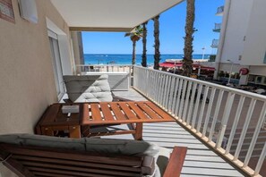 A balcony with a wooden table and chairs, a cushioned bench, and a view of the beach and ocean. - Apartment on the beachfront in La Fossa with ocean and pool views. (Calpe)