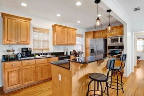 A modern kitchen with wooden cabinets, stainless steel appliances, and a central island with bar stools. - Summerville Suite (Mobile)