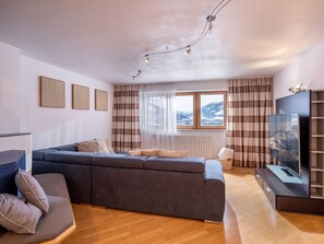 A modern living room with a sectional sofa, a flat-screen TV, and a window with a mountain view. - Holiday home with panoramic views (Hopfgarten im Brixental)