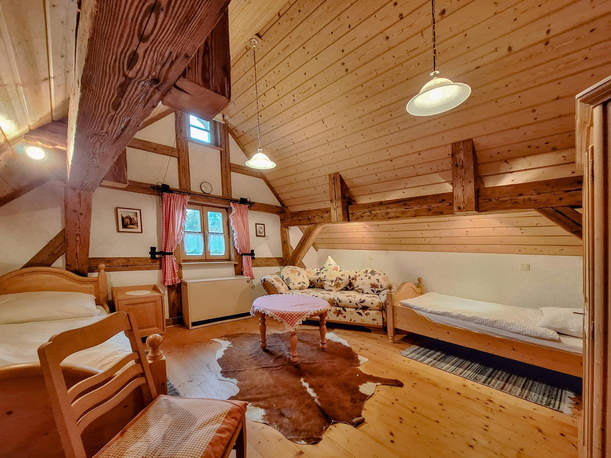 Interior acogedor de una cabaña con techo de madera, un sofá, una cama, una silla y un tapiz de cuero de vaca.