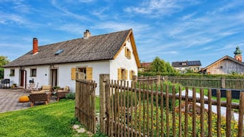 A white house with a sloped roof, a wooden fence, and a garden with yellow flowers.