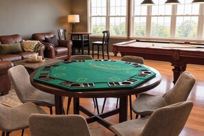 Una stanza con tavolo da biliardo, un tavolo da poker con feltro verde, arredamento in pelle e vista attraverso ampie finestre.
