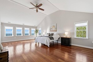 Un'ampia camera da letto con un letto grande, una ventola a soffitto e numerose finestre che offrono vista sul panorama esterno.