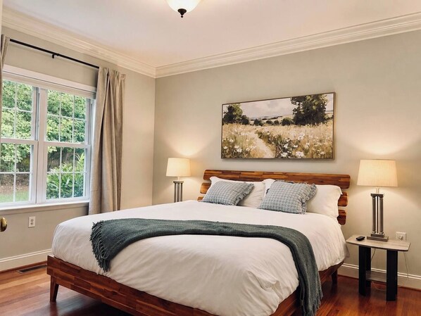 A bedroom with a wooden bed, two bedside tables, a window with curtains, and a painting on the wall.