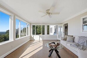 A spacious room with large windows, a ceiling fan, a glass coffee table, and a white sofa.
