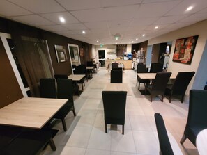 Een restaurant met meerdere tafels en stoelen, een balie en een keuken op de achtergrond.