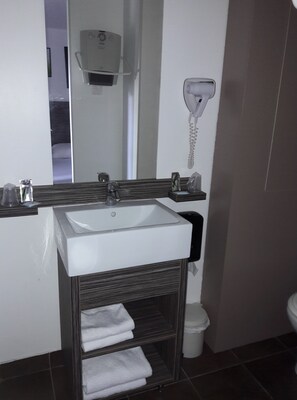 Een badkamer met een witte wastafel, een spiegel, een handdoekrek en een handdroger.
