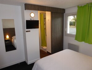 Een hotelkamer met een bed, een televisie, een douche en een raam met gordijn.