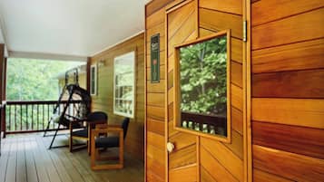A wooden cabin with a porch, a swing chair, and a small table.