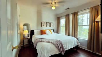 A bedroom with a bed, a ceiling fan, a nightstand with a lamp, and a window with curtains.