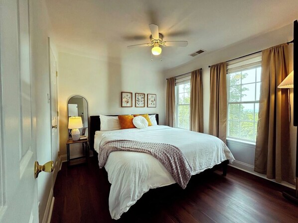 A bedroom with a bed, a ceiling fan, a nightstand with a lamp, and a window with curtains. - The RidgeView Retreat-HotTub Sauna Forest Patio (Harpers Ferry)