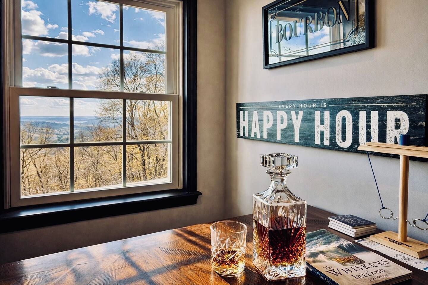 A room with a large window, a whiskey decanter, glasses, books, and a 'Happy Hour' sign.