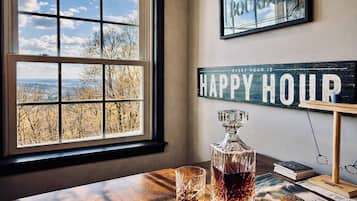 A room with a large window, a whiskey decanter, glasses, books, and a 'Happy Hour' sign.