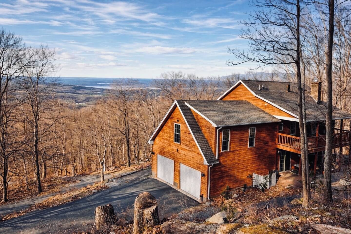 A two-story wooden house with a garage, a balcony, and a view of a forested landscape.