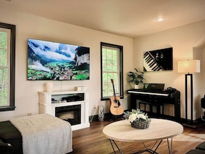 Un salon avec une cheminée, un téléviseur, un piano, une guitare et une table basse ronde.