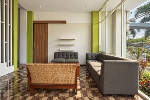 Un interior moderno con un sofá, una silla y una mesita. Se observa una puerta de madera y una pared blanca con estanterías.