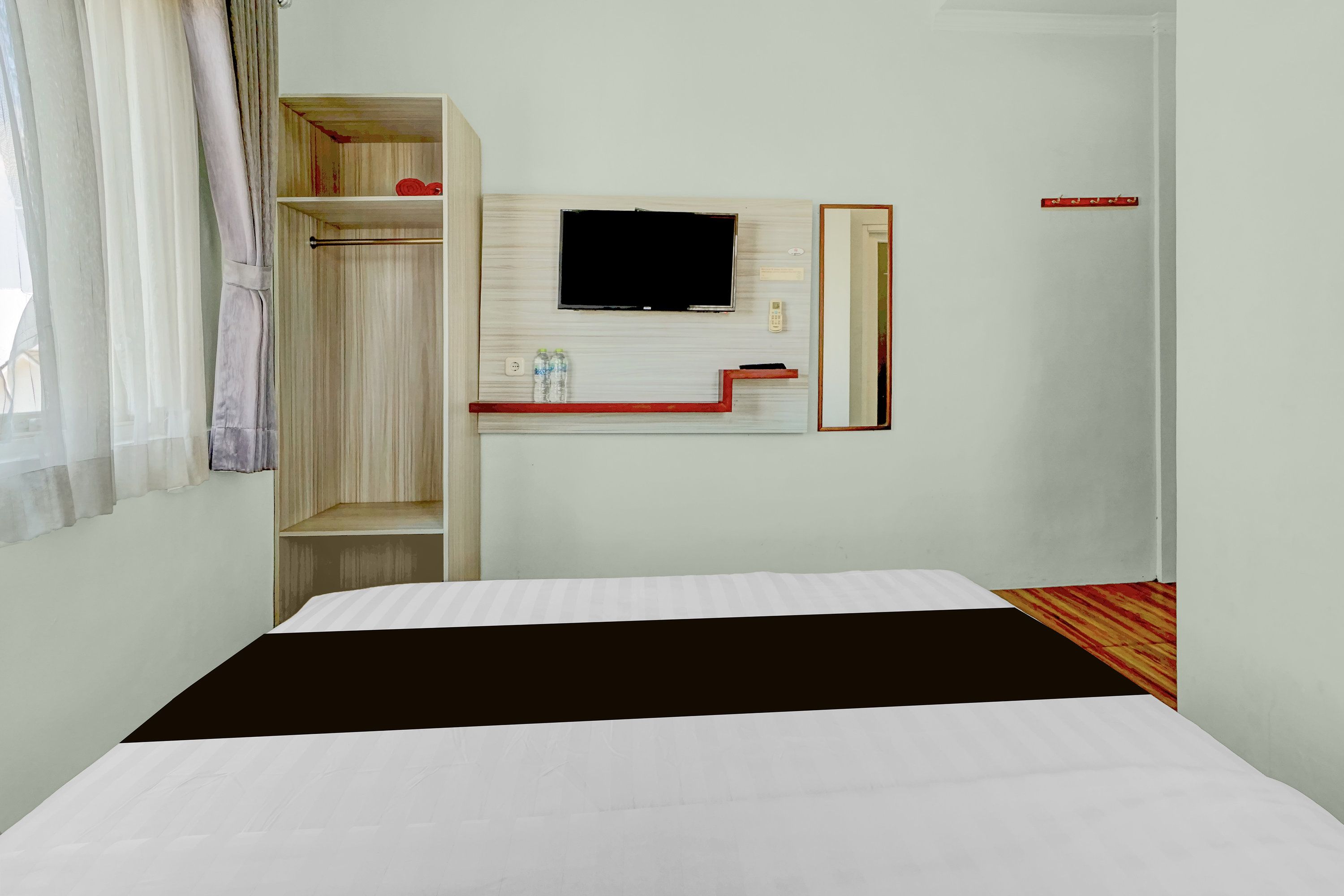A hotel room with a bed, a TV mounted on the wall, a built-in wardrobe, and a small table with a mirror.