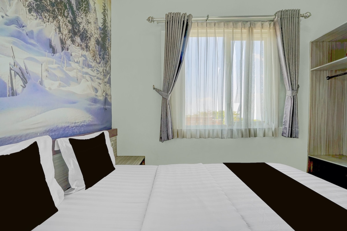 Habitación de hotel con cama, un cuadro en la pared y una ventana con cortinas.