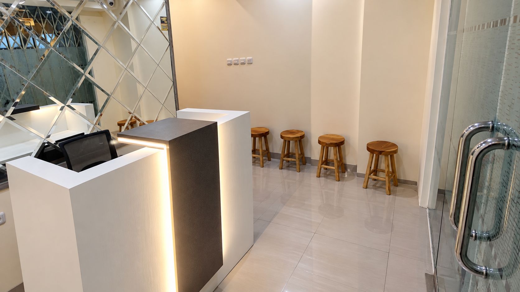 Un área de recepción moderna con un escritorio blanco, taburetes de madera y un panel de vidrio.