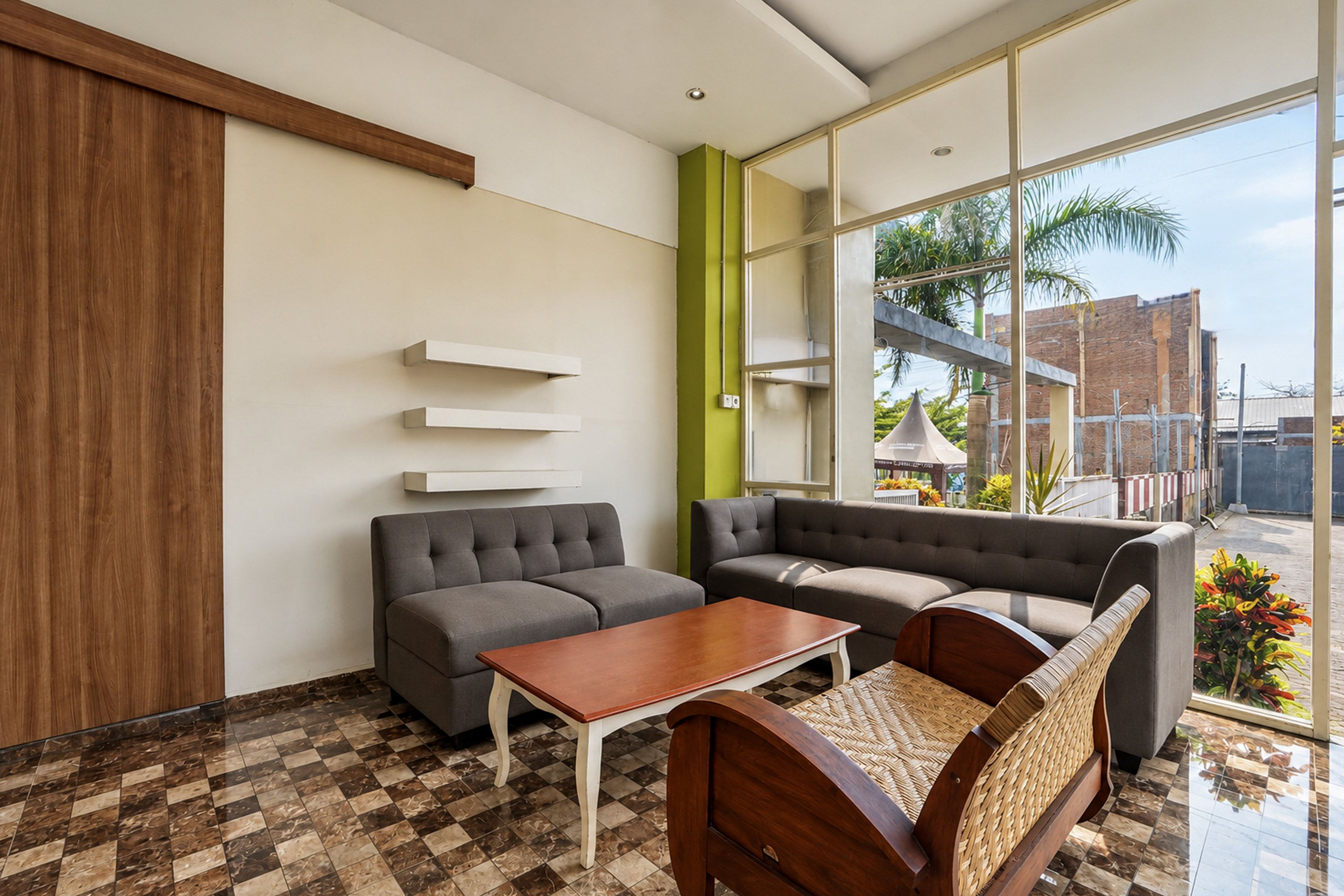 A modern hotel lobby with a checkered floor, grey sofas, a wooden table, and a large window offering a view of the outside.