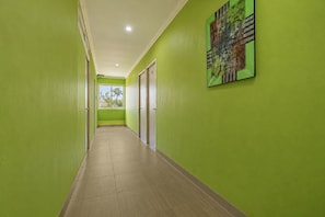 Un pasillo con paredes verdes, piso de baldosas y una puerta al final.