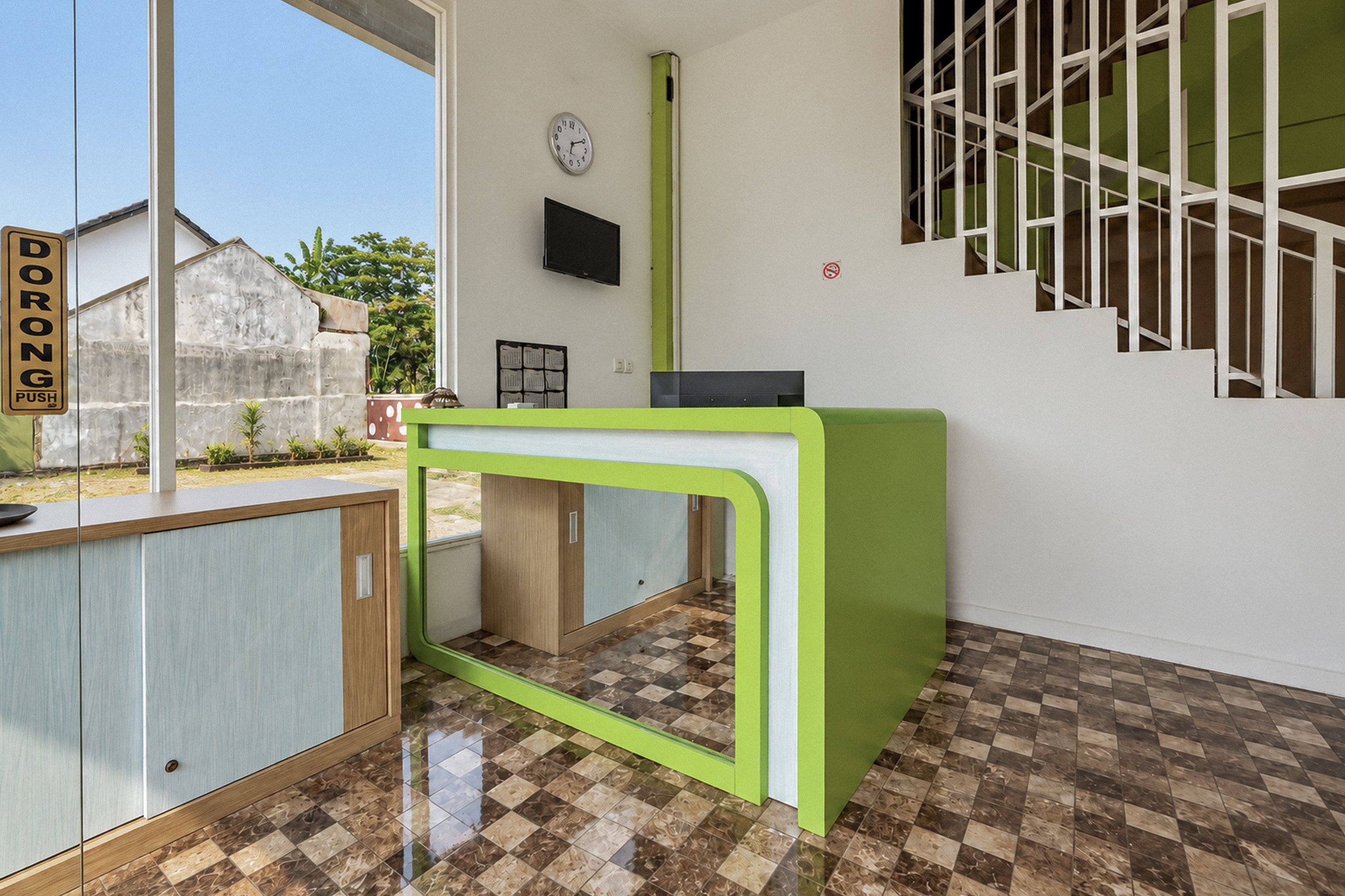 A reception desk with a green frame, a clock on the wall, and a staircase to the right.
