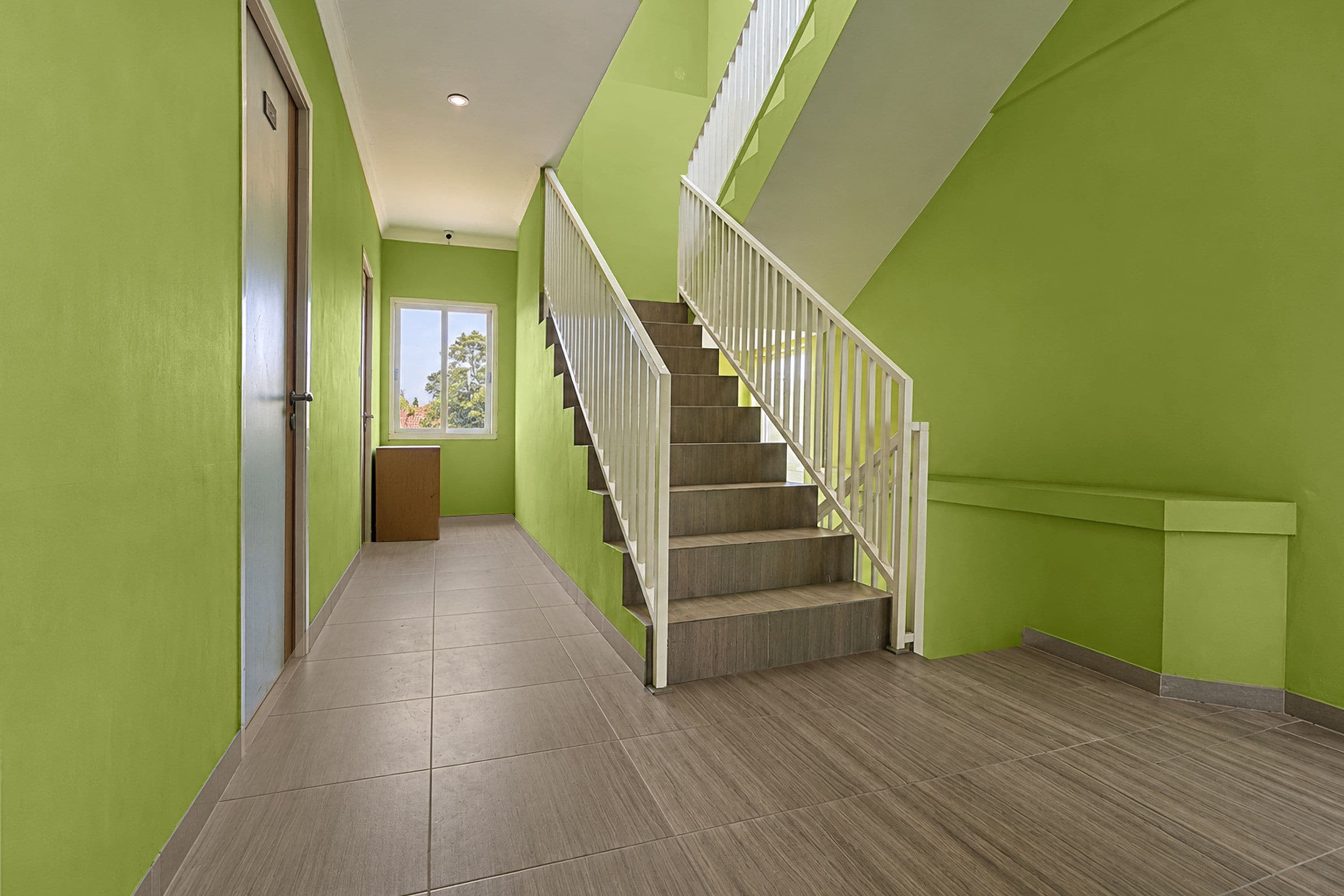 A hallway with a staircase, green walls, and a door on the left.