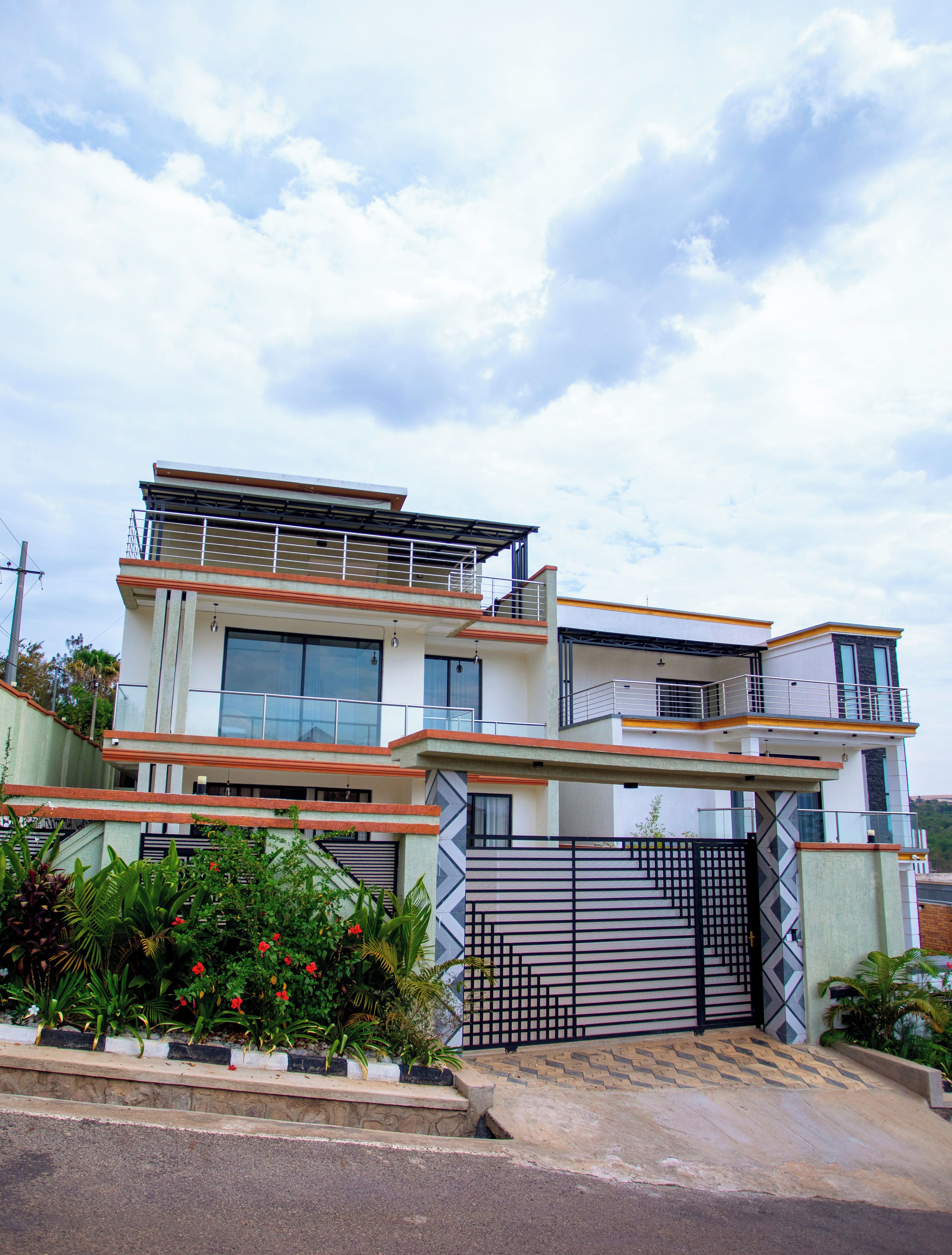 A modern two-story house with a gated entrance, large windows, and a balcony.