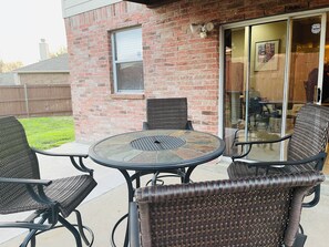 A patio with a round table and four wicker chairs, a brick wall, and a sliding glass door leading to an interior space. -  Spacious 2-story 6-bedroom House Perfect for Families & Work Groups (Melissa)