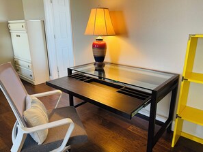 A room with a glass-top table, a chair with a cushion, a lamp, a white cabinet, and a yellow cabinet. -  Spacious 2-story 6-bedroom House Perfect for Families & Work Groups (Melissa)
