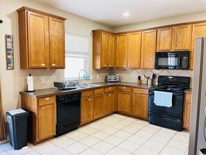 A kitchen with wooden cabinets, a black microwave, a stove, and a dishwasher. -  Spacious 2-story 6-bedroom House Perfect for Families & Work Groups (Melissa)
