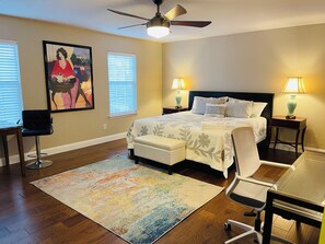 A bedroom with a bed, two bedside tables with lamps, a desk with a chair, a ceiling fan, and a large painting on the wall. -  Spacious 2-story 6-bedroom House Perfect for Families & Work Groups (Melissa)