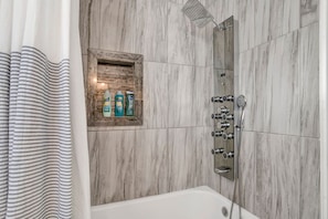 A bathroom with a shower, a bathtub, and a wooden medicine cabinet with toiletries. - Southern Comfort (Mobile)