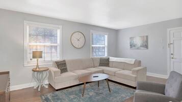 A living room with a beige sectional sofa, a round coffee table, a side table with a lamp, and a blue rug.