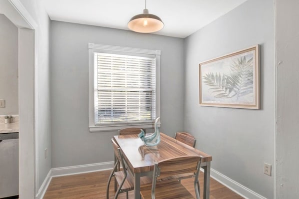 Un comedor con una mesa y sillas de madera, una ventana con persianas y un cuadro en la pared.