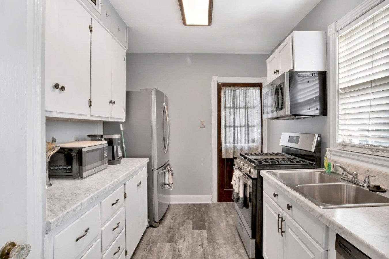 A compact kitchen with white cabinets, a refrigerator, a microwave, a stove, and a sink.