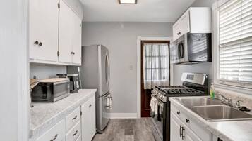 A compact kitchen with white cabinets, a refrigerator, a microwave, a stove, and a sink.