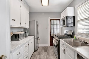 Cocina compacta con armarios blancos, refrigerador, microondas, estufa y pileta.