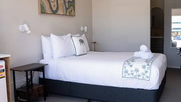 A bedroom with a bed, a desk, a ceiling fan, and a painting on the wall.