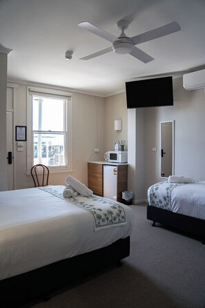 A hotel room with two beds, a ceiling fan, a TV mounted on the wall, a microwave, and a window with a view of the outside. - The Palms Tocumwal (Tocumwal)