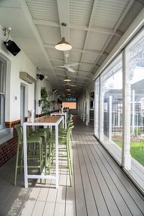 A covered outdoor dining area with tables and chairs, a ceiling fan, and a view of the outside.