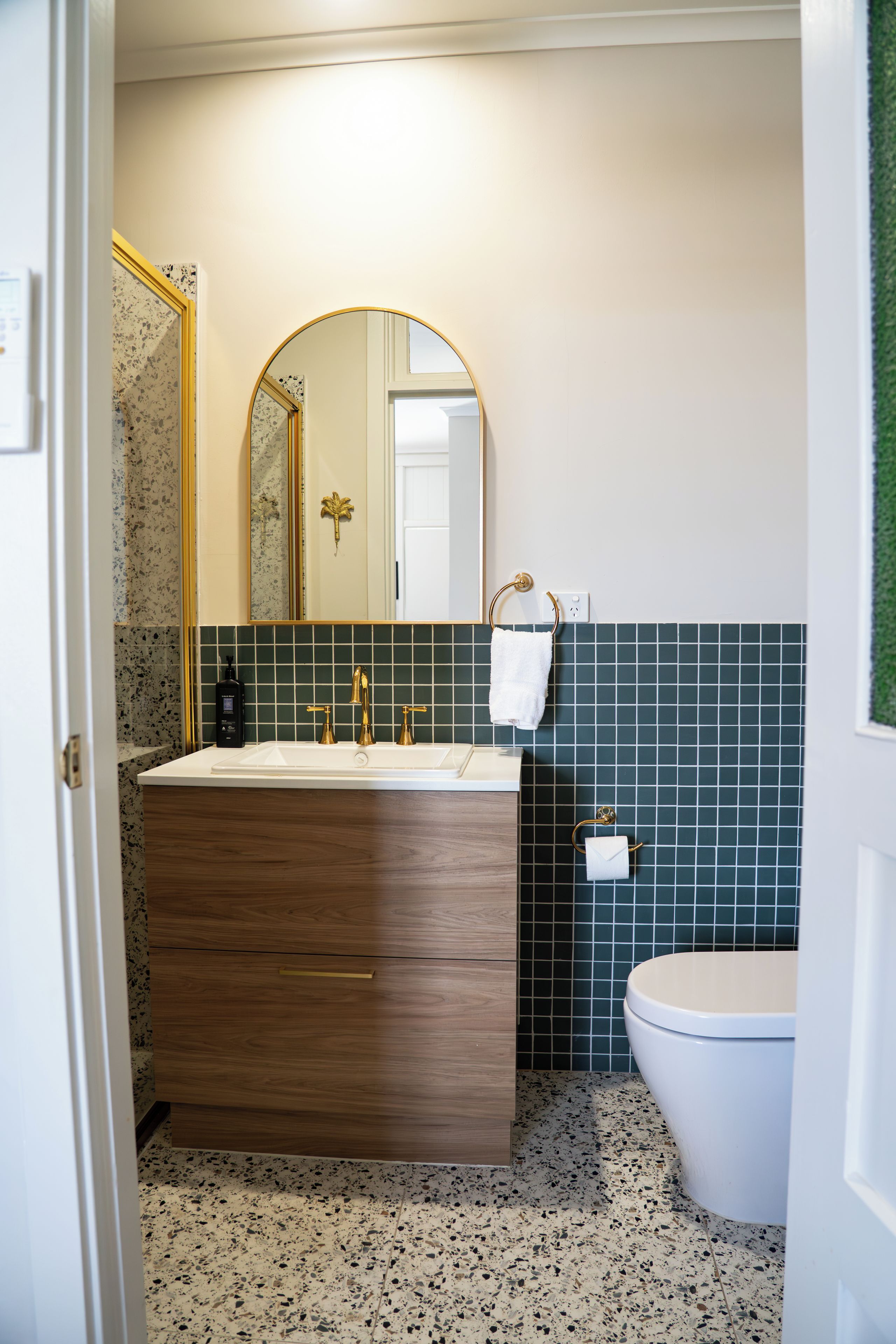 Un baño con tocador de madera, lavamanos independiente, inodoro y espejo con marco dorado.
