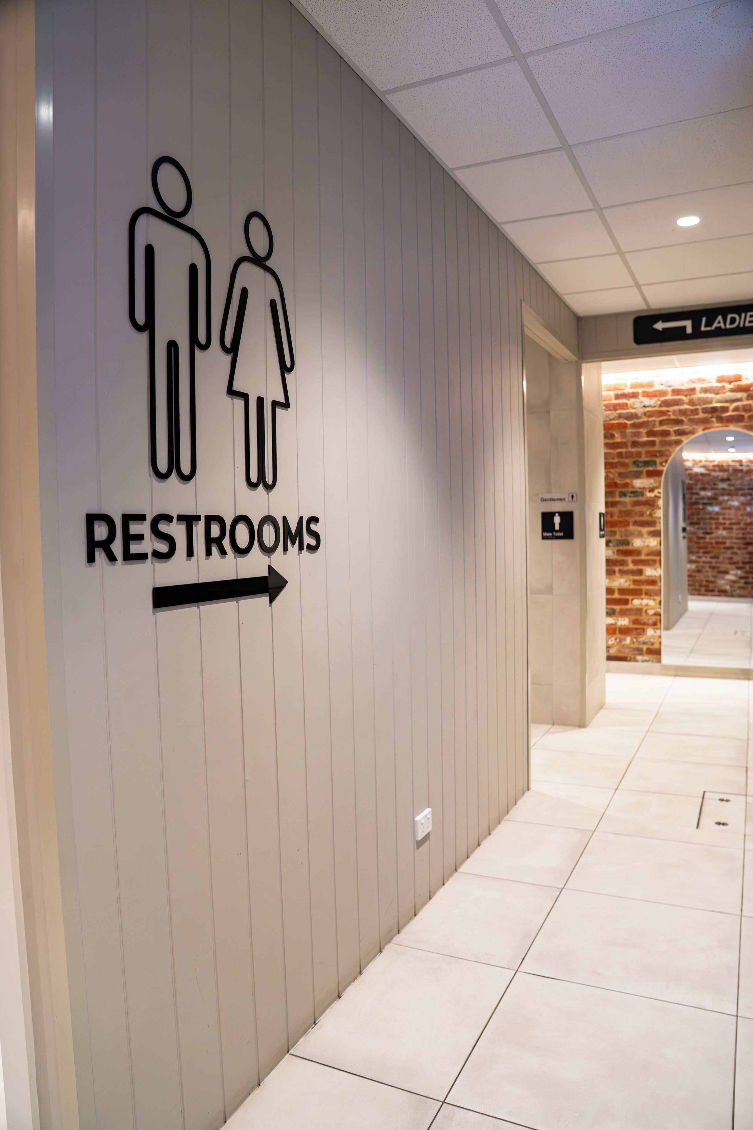 A directional sign for restrooms with a male and female symbol and an arrow pointing to the right.