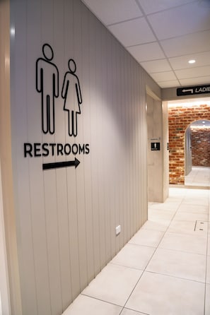 A directional sign for restrooms with a male and female symbol and an arrow pointing to the right.