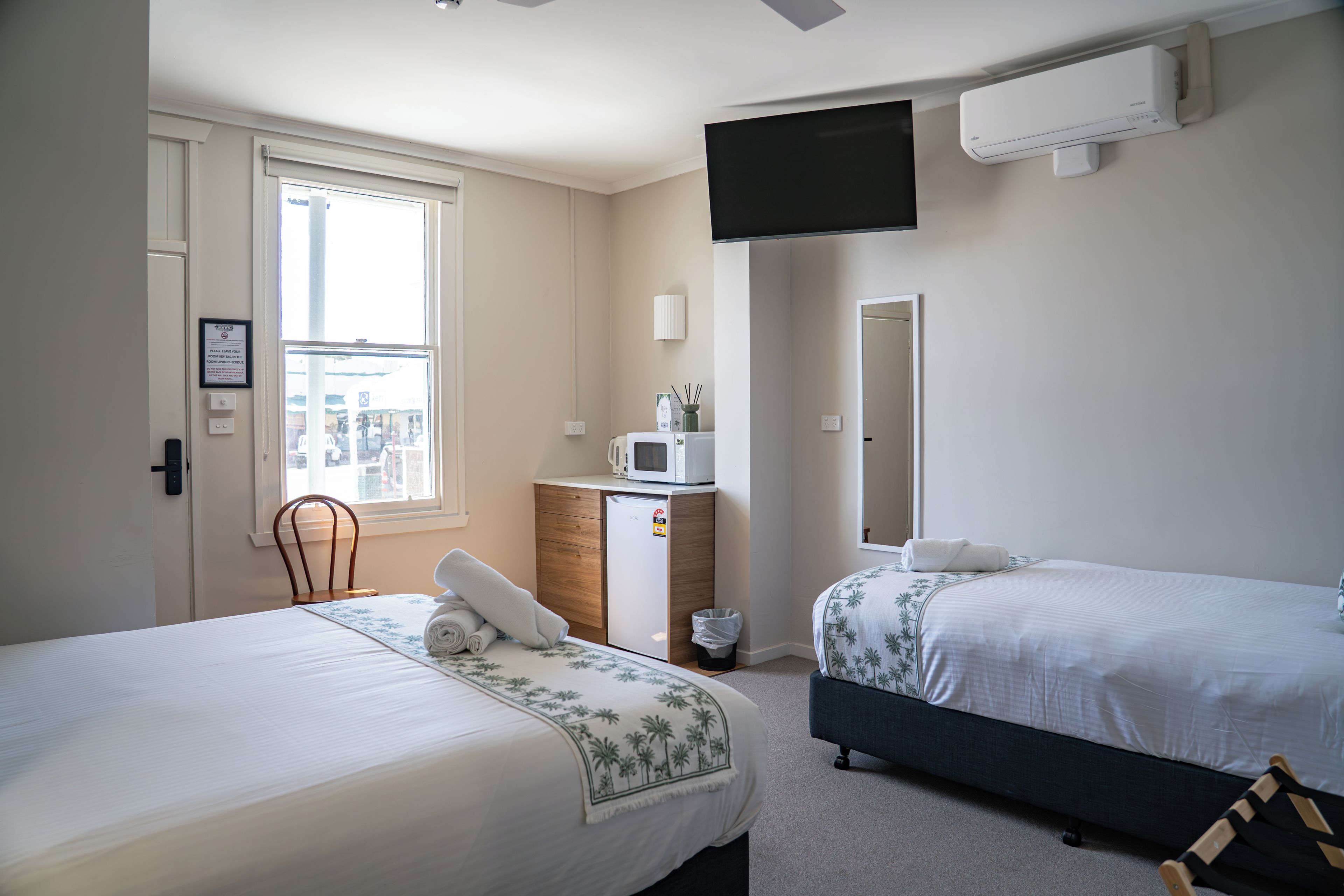 A hotel room with two beds, a desk with a microwave, a TV, and a window with a view of the outside.