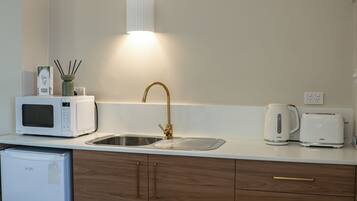A modern kitchen with a built-in microwave, a stainless steel sink, and a kettle on the countertop.
